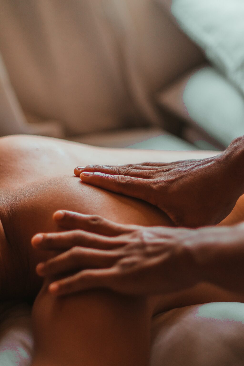 Massage therapist applying focused pressure to the left shoulder area of a person lying face down during a relaxing massage session.